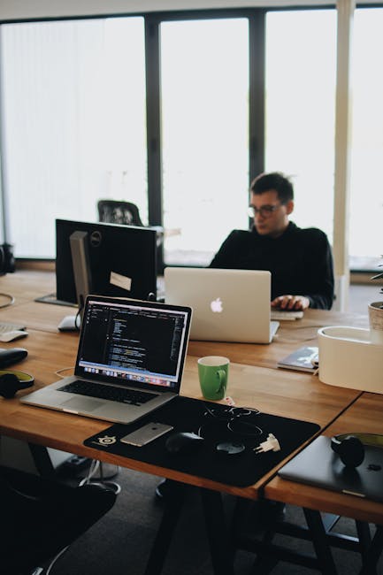 A web developer working on code in a modern office setting with multiple devices.